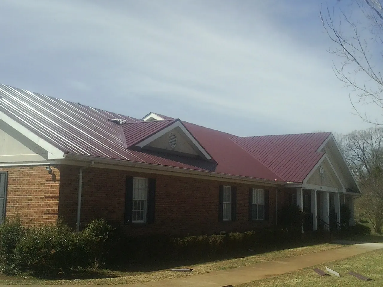 Red metal roof with gabled entries on a long brick building, from a Hail Damage Roof Repair job in West Elizabeth