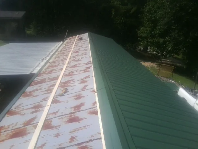 Old rusted panels beside newly installed green metal roofing — Wind Damage Roof Repair by Roofing Brothers in West Elizabeth