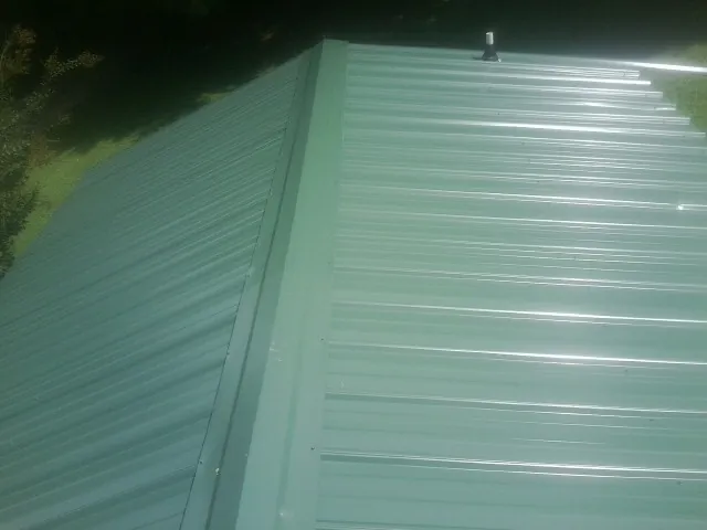 New green metal panels meeting at the ridge of a roof — Flat Roof Repair work by our crew in West Elizabeth