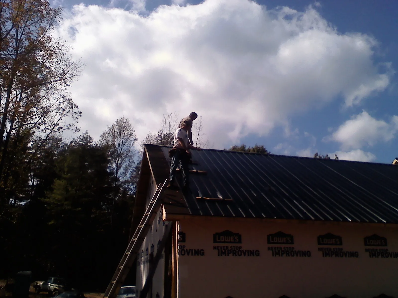 Roofer fastening dark metal panels high against a cloudy sky, from a Roof Inspection job in West Elizabeth