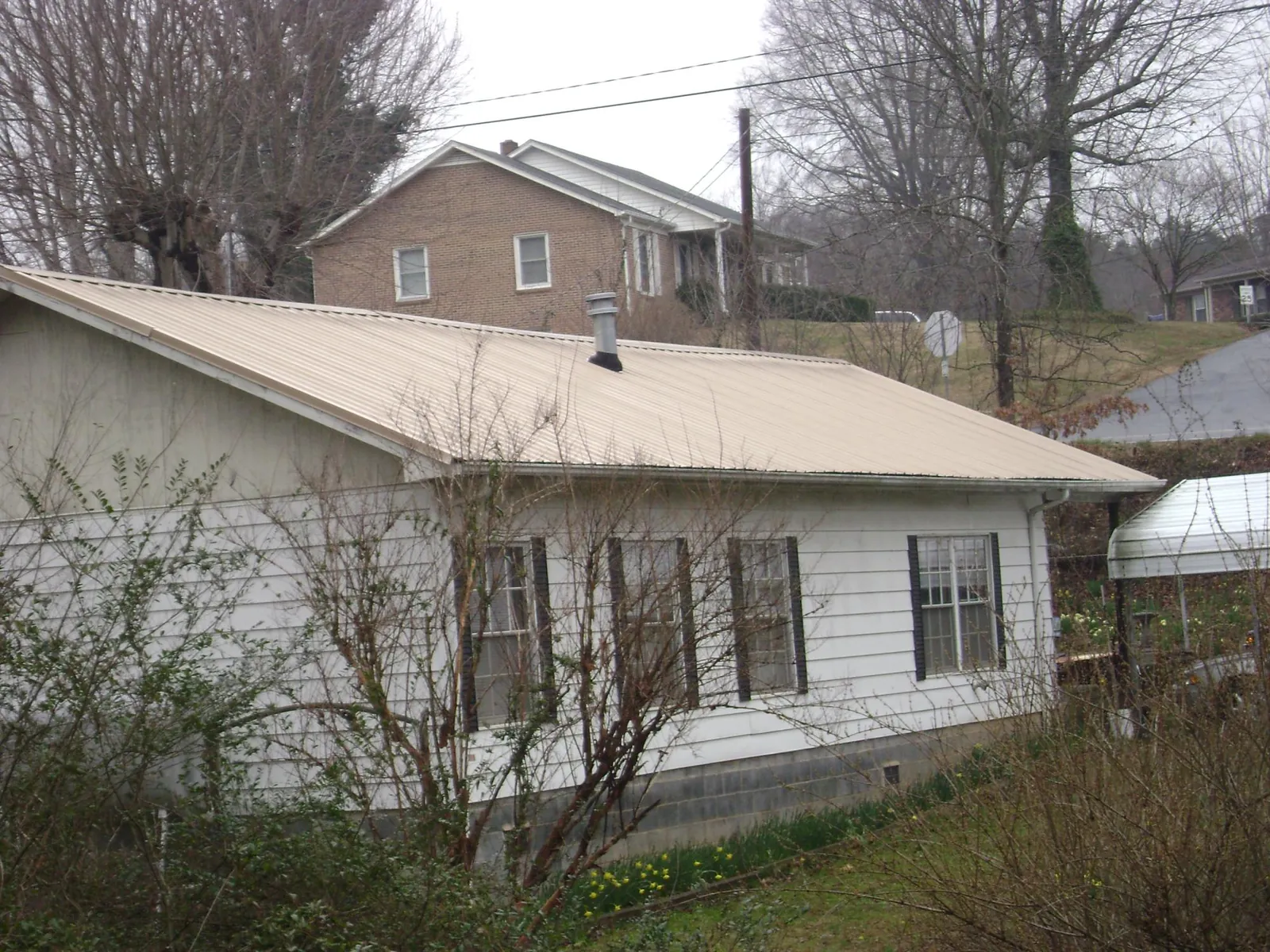 Tan metal roof on a white sided house set into a hillside — Commercial Roofing by Roofing Brothers in West Elizabeth